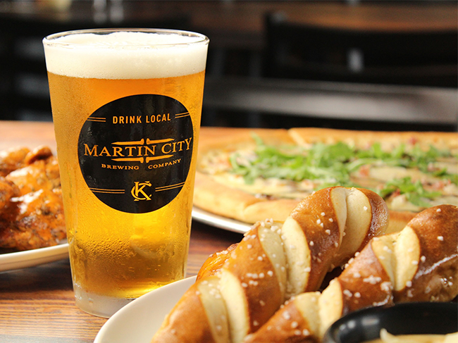 Draft beer in pint glass with soft pretzels and pizza